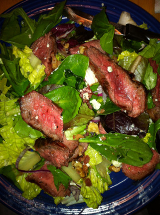 Medium rare flat iron steak on mixed greens with walnuts, red onion slivers and white balsamic vineg